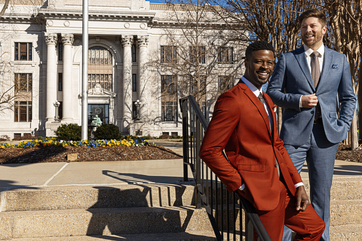 Two models outside a courthouse, one in a rust suit and one in a light blue suit