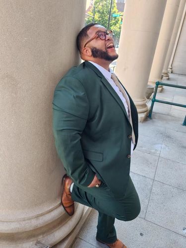 Customer Chad D. wearing the Forest Green 2 Button Suit, leaning against a column