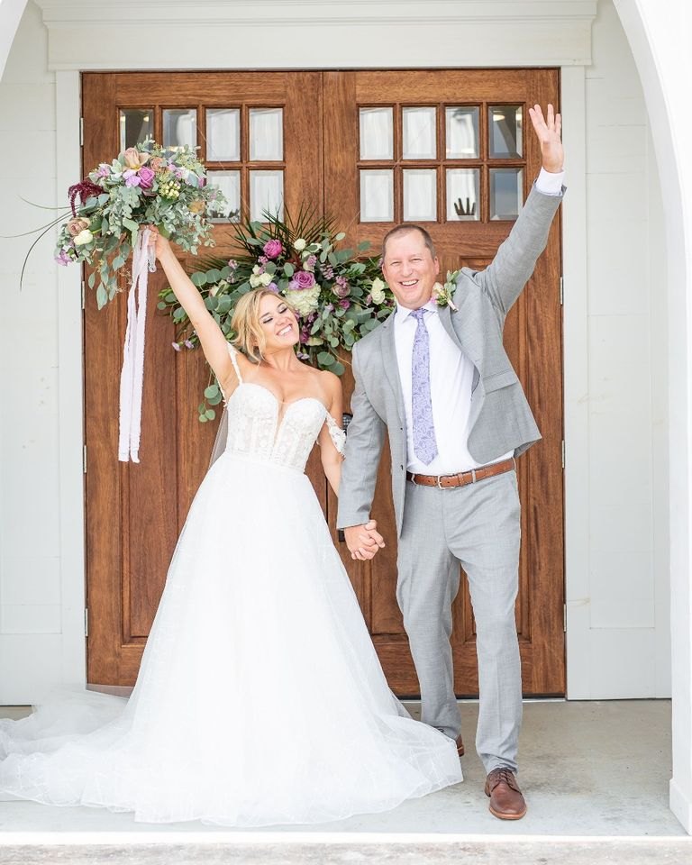 A groom in a light gray suit and his bride celebrating in front of chapel doors