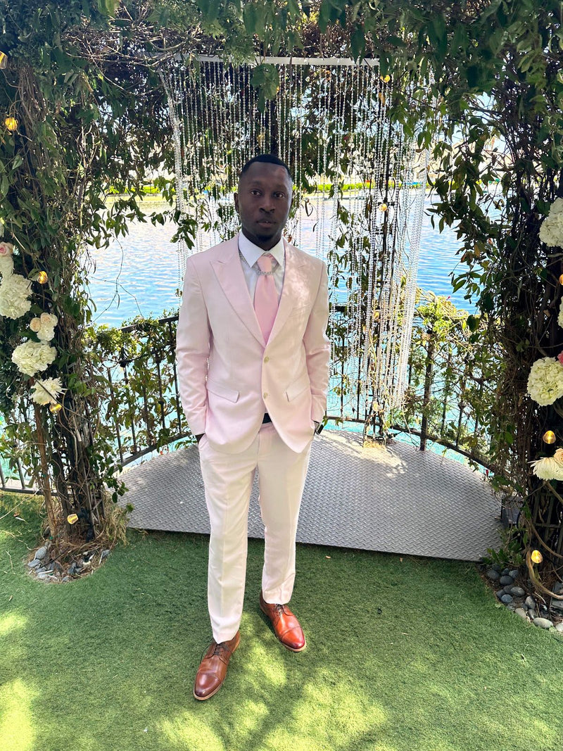 Groom Marcus J. in the Blush Pink 2 Button Suit in front of a floral wedding arch