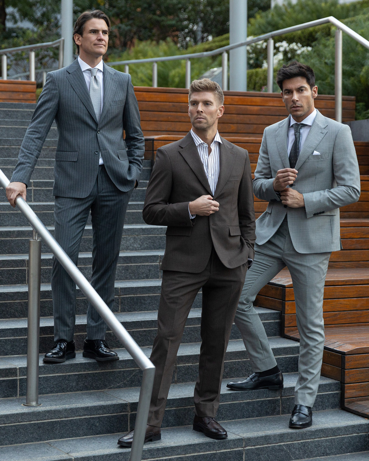 Three models on outdoor steps in gray pinstripe, brown and light gray suits